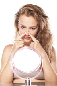 A young blonde woman touching her nose and looking in the mirror